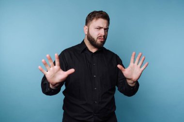 Siyah tişörtlü adam, iki elini de mavi arka planda tutarak dur diyor..