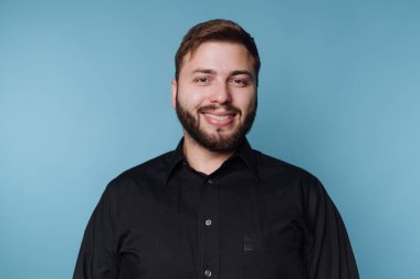 Mavi arka planda siyah gömlekli, gülümseyen adam.