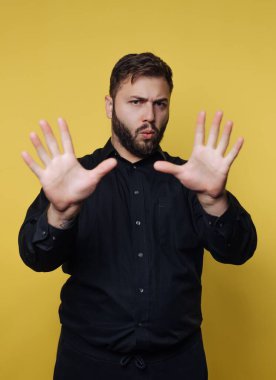 Siyah tişörtlü adam ellerini sarı arka planda tut..