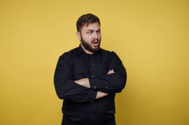 Sarı arka planda kolları çapraz siyah gömlekli adam..