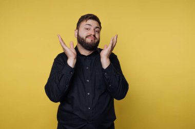 Siyah gömlekli adam sarı arka plana karşı omuz silkiyor..