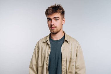 Sade bir arka planda sıradan giyinmiş genç bir adam..