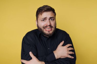 Siyah gömlekli bir adam sarı arka planda endişeli görünür..