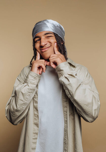Young man with braided hair and bandana smiling playfully.