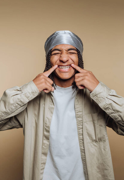 Young person with braces smiling and pointing at teeth.