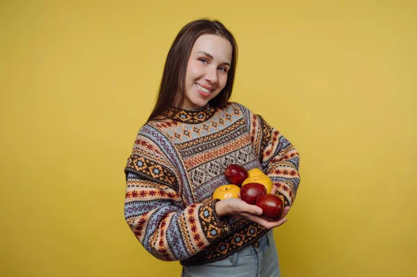 Sarı arka planda elmaları tutan gülümseyen kadın.
