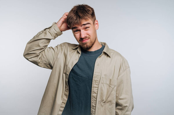 Young man scratching head, looking confused, wearing casual clothes.