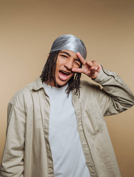 Young person with braided hair and a durag making a peace sign.