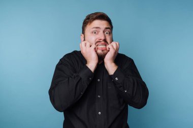 Mavi bir duvara karşı duran bir adam var. Yüzünde elleri ve korku belirtileri gösteren endişeli bir ifade var. Güçlü bir duygusal tepki yakaladığı an.