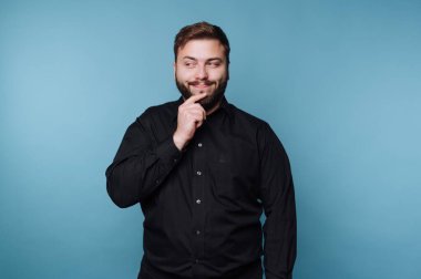 Stüdyoda mavi bir geçmişi olan bir adam var. O bir gülümseme ve eli çenesinde dinlenen bir düşünce duraksaması var. Dekor modern ve basit bir stüdyo ortamını gösteriyor..