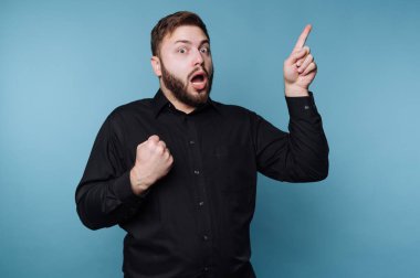 Stüdyoda mavi bir geçmişi olan bir adam var. Onun kısa bir sakalı var ve siyah bir gömlek giyiyor. Bir parmağını kaldırıp yumruk atarken ifadesi heyecanını gösteriyor..