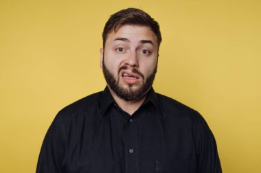 Bir adam parlak sarı bir arka plana karşı duruyor. Onun sakalı ve şakacı bir ifadesi var. O, aptal bir yüzle doğrudan kameraya bakıyor..