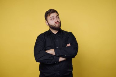 Sarı bir duvarın önünde bir adam duruyor. Kollarını kavuşturmuş ve düşünceli bir ifade takınıyor. Ortalık aydınlık ve sade, dikkat dağıtıcı bir şey yok..