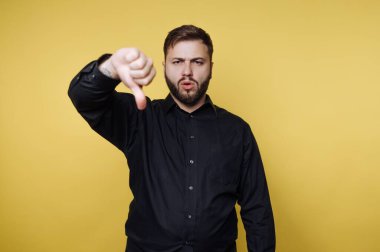 Sarı bir duvarın önünde duran bir adam baş parmak hareketi yapıyor. Onaylamadığını ya da tatminsiz olduğunu gösteriyor. Onun ciddi yüzü mesaja ekleniyor..