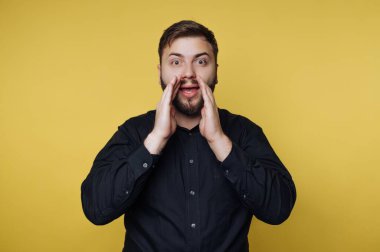 Bir adam sarı bir duvara karşı duruyor. O, seslenirken ellerini ağzına kaldırır. Onun ifadesi heyecanı gösteriyor. Bu sahne basit ve doğrudan..