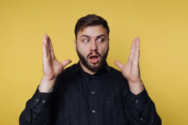 Bir adam, elleri havada ve yüzünde şok olmuş bir ifadeyle parlak sarı bir arka planın önünde duruyor. Beklenmedik bir habere ya da şaşırtıcı bir olaya tepki veriyor gibi görünüyor..