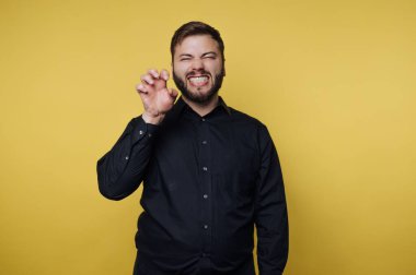 Sarı bir duvarın önünde şakacı bir pençe hareketi yapan bir adam. Gülümser, neşeli ve enerjik bir atmosfer yaratır..