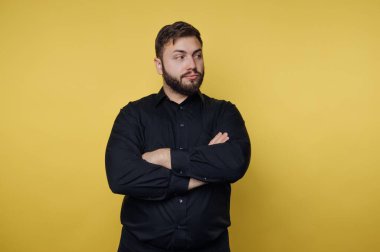 Bir insan kollarını kavuşturup yan tarafa bakar. Arka plan parlak sarı. Bu sahne gün içinde bir stüdyoda geçiyor..