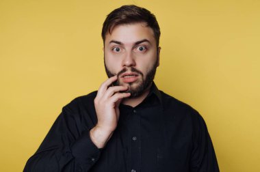 Bir adamın yüzünde eli ile şaşırmış bir ifade vardır. O, parlak sarı bir arka plana karşı duruyor. Adam beklenmedik bir şeye tepki veriyor gibi görünüyor..