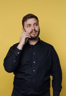 Sarı arka planda bir adam duruyor. Kulağına bir telefon dayadı ve konuşurken gülümsedi. Keyifli bir konuşma yapıyor gibi görünüyor..