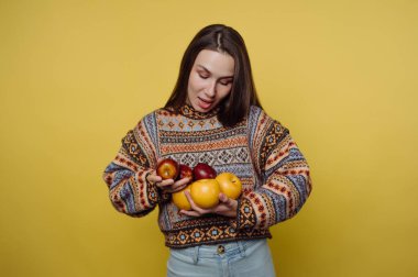 Sarı bir geçmişi olan genç bir kadın stüdyoda duruyor. Ellerinde birkaç elma ve limon tutuyor. Meyvelere faiziyle bakıyor..