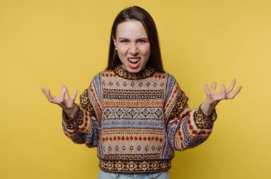 Bir kadın öfkesini ve hayal kırıklığını yüzünü asarak ve ellerini kaldırarak gösterir. O, desenli bir kazak giyiyor. Arkaplan parlak sarı, canlı bir ortam yaratıyor..