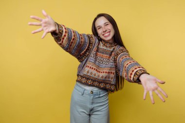 Uzun saçlı genç bir kadın stüdyoda parlak sarı bir arka plana karşı duruyor. Kollarını açıyor ve gülümsüyor, neşe ve heyecan gösteriyor. Işık uzayda parlaktır..