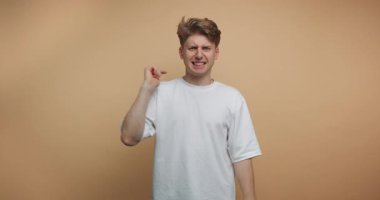 Bir adam stüdyoda duruyor ve kamerayı işaret ediyor. Farklı el hareketleri sergiliyor. Arka plan sade. Gündüzleri ışık parlıyor..