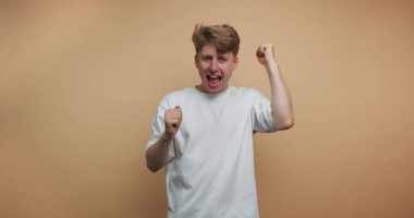 Genç bir adam dans ediyor ve turuncu bir arka plan önünde hareketler yapıyor. Hareketleri ve ifadeleriyle neşe ve heyecan gösteriyor..