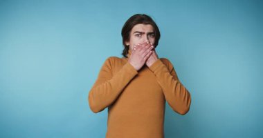 Bir adam mavi bir arkaplan önünde çeşitli yüz ifadeleri sergiler. Elleriyle ağzını kapatırken şaşkın, düşünceli ve kafası karışmış görünüyor..