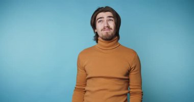 Bir adam dört karede el hareketleriyle düşüncelerini ifade ederken görülüyor. Ayarın mavi bir arka planı var. İçerideyken farklı tepkiler veriyor..