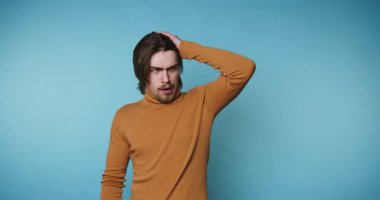 Stüdyoda mavi bir geçmişi olan bir adam var. Kafasına dokunuyor ve kameraya bakarken farklı ifadeler gösteriyor. Gündüz vakti..