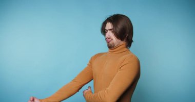 Kahverengi kazak giyen bir adam farklı spor faaliyetleri gösterir. Kaslarını esnetip esneterek dört kare şeklinde poz veriyor. Arkaplan sade mavi.