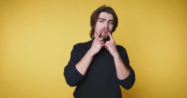 Stüdyoda duran bir adam sarı arka planda çeşitli yüz ifadelerini gösteriyor. Yüz hareketlerini eğlenceli bir şekilde geliştirmek için ellerini kullanıyor. Oturum vücut dilinde yaratıcılığı gösterir.