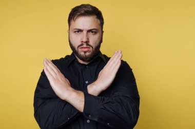 Genç bir adam göğsünün önünde kollarını kavuşturup ciddi bir ifade sergiliyor..