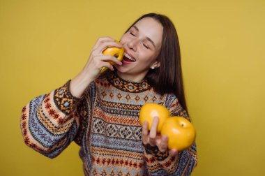 Neşeli bir kadın bir elinde üç sarı elma tutarken diğerinden bir ısırık alıyormuş gibi yaparak taze meyvelerden zevk alır. Parlak sarı arkaplan enerji katar.