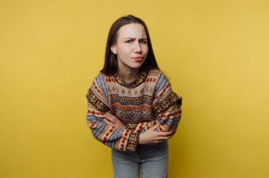 Kolları çapraz duran, renkli bir kazak giyen bir kız karmaşık desenler sergiliyor..