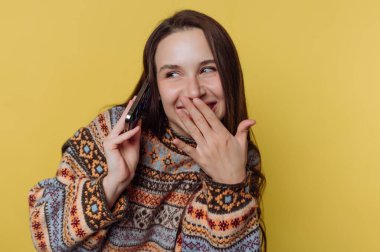 Parlak, rahat, desenli bir kazak giymiş genç bir kadın gülümsüyor ve telefonunu kulağına dayıyor. Neşeli ifadesi, samimi bir anı paylaştığını, eğlenceli bir sohbetten hoşlandığını gösteriyor..