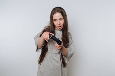 Genç bir kadın, kendine güvenen bir gülümseme ve eğlenceli bir tavır sergileyen bir oyun kontrolörüyle şakacı bir şekilde poz veriyor. Uzun saçları, içeride oyun oynamaktan zevk aldığı için özgürce akıyor..