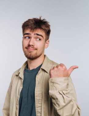 Genç bir adam rahat bir şekilde dikiliyor, sıradan bir kıyafet giyiyor. Yana bakarken yüzsüz bir sırıtışla, eğlence ya da eğlenceli bir davetiye öneriyor..