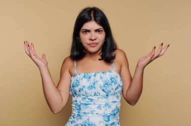 Genç bir kadın, yumuşak ve sessiz bir arkaplanda dururken şaşkınlığını ifade eder. Şaşırmış görünüyor, ellerini hafifçe kaldırmış sanki etrafındaki dünyayı sorguluyormuş gibi, merak duygusu yaratıyor..