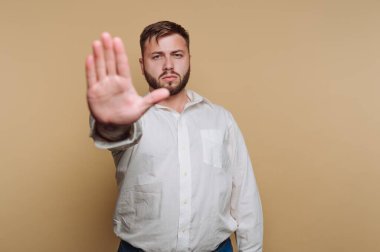 Kendinden emin bir adam sıcak, tarafsız bir arkaplana karşı duruyor ve bir meydan okuma jesti olarak elini kaldırıyor. Onun ciddi ifadesi ana yoğunluk katıyor..