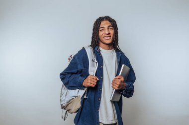 Genç bir öğrenci parlak bir ışıkla duruyor, bir omzunda sırt çantasıyla sıradan bir kıyafet giyiyor. Bir dizüstü bilgisayar ve coşkuyla ışıldıyor, öğrenme gününe hazır..