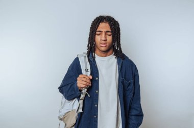 Sakin ve sessiz bir yerde, genç bir adam, örgülü saçlarıyla sırt çantasını taşırken hareketsiz duruyor. Gözleri kapalı, düşüncelere dalmış, hayatın anlarını yansıtıyor..