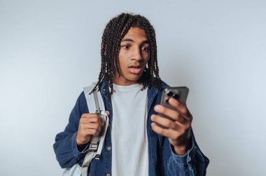 Genç bir adam evde rahat bir ortamda dikiliyor. Dikkatini akıllı telefonuna veriyor..