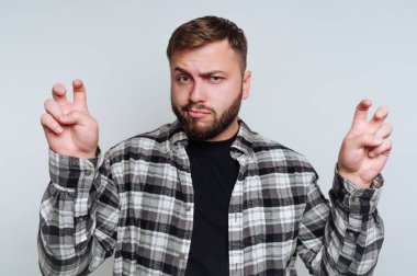 Bir adam basit bir arka plana karşı duruyor, modaya uygun bir gömlek giyiyor. Küstahça bir ifadeyle, eğlenceli bir şekilde parmaklarıyla jest yapıyor, kendine güveni ve mizahı yansıtıyor..