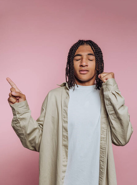 A young man with stylish braided hair dances with enthusiasm in front of a vibrant pink backdrop. His joyful gestures showcase a sense of freedom and positivity, capturing a moment of pure happiness.