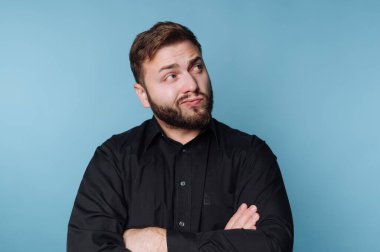 Sakallı ve neşeli bir ifade takınan bir adam kollarını kavuşturup merak ve özgüvenin bir karışımını sergiliyor. Arkaplan, sahnenin havasını yükselten parlak bir mavi..