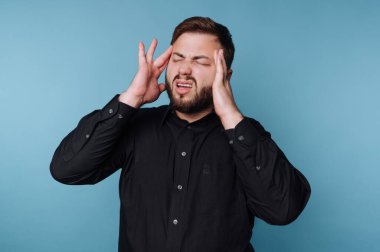 Genç bir adam elleri başının üstünde duruyor, sakin mavi bir arka planda hayal kırıklığı ya da stres belirtileri gösteriyor. Yüzündeki ifade, derin bir iç mücadele ve meydan okuma anını yansıtıyor..