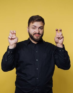A man wearing a black shirt stands confidently in front of a vivid yellow background, playfully gesturing with his fingers as he smiles. This lively scene radiates fun and energy.